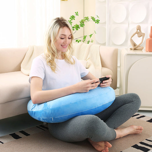 The U-shaped comfort pillow rests on a desk, providing arm support for someone working on a laptop.